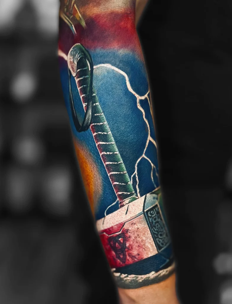 Kolorowy realistyczny tatuaż przedstawiający Mjolnir – młot Thora z błyskawicami wykonany przez Bartka w Studio Fortuna Tattoo w Warszawie.