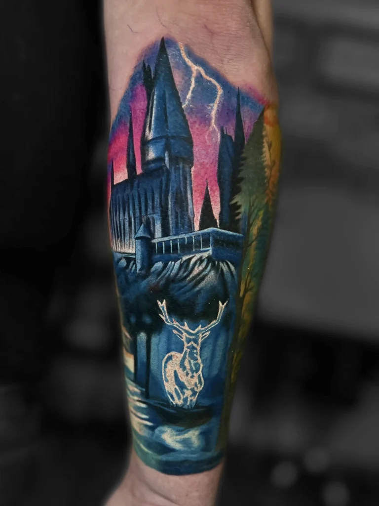 Kolorowy realistyczny tatuaż inspirowany Harrym Potterem z zamkiem Hogwart i Patronusem jelenia wykonany przez Bartka w Studio Fortuna Tattoo w Warszawie.
