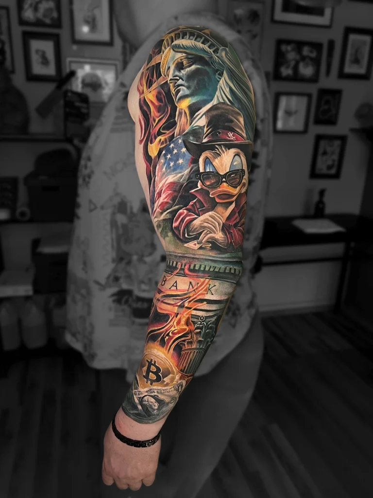 Kolorowy realistyczny rękaw z motywami Statuy Wolności, Sknerusa McKwacza, Bitcoina i dolara wykonany przez Bartka w Studio Fortuna Tattoo w Warszawie.