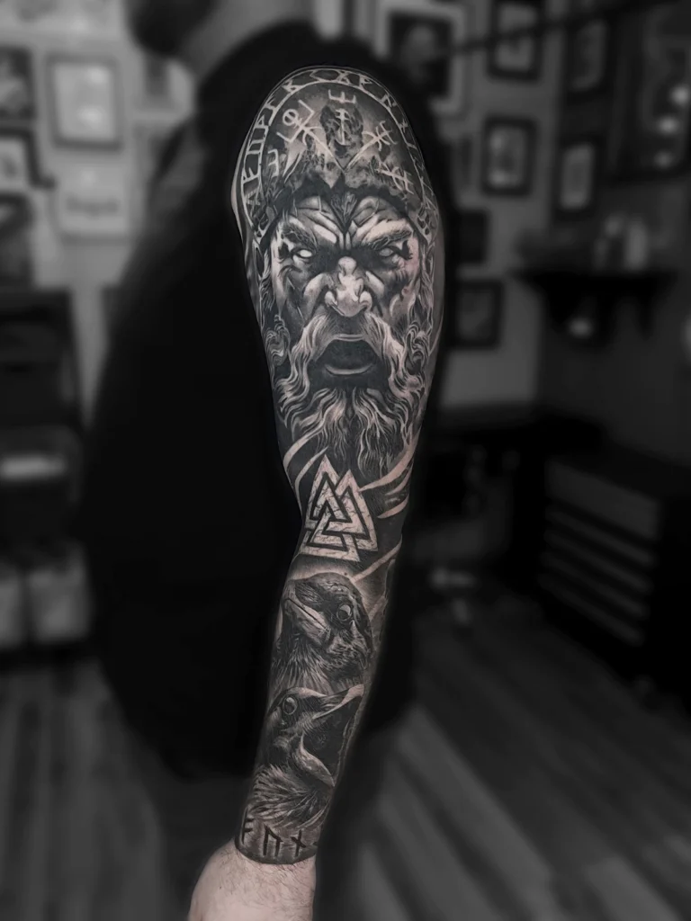 Tatuaż realistyczny black & grey przedstawiający Odyna, kruki Huginn i Muninn oraz symbole nordyckie wykonany przez Bartka Fortunę w Warszawie.